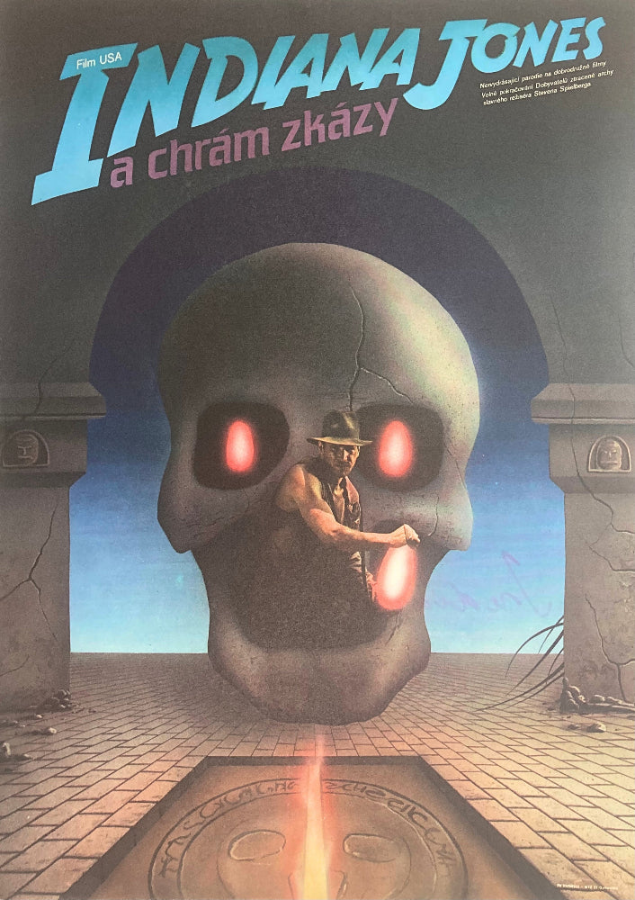 Man in a hat standing in front of a large skull with glowing red eyes.