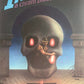 Man in a hat standing in front of a large skull with glowing red eyes.